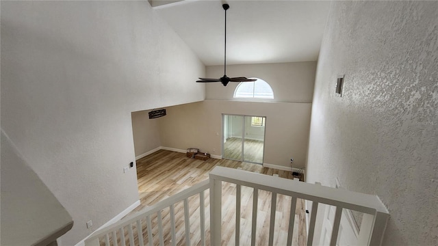 interior space featuring ceiling fan, a textured wall, a high ceiling, wood finished floors, and baseboards