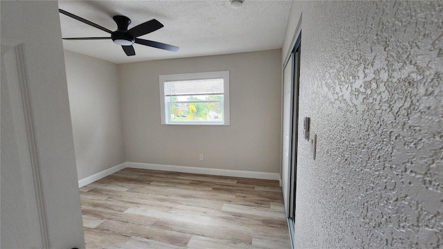 spare room featuring light wood-style floors, a ceiling fan, baseboards, and a textured ceiling