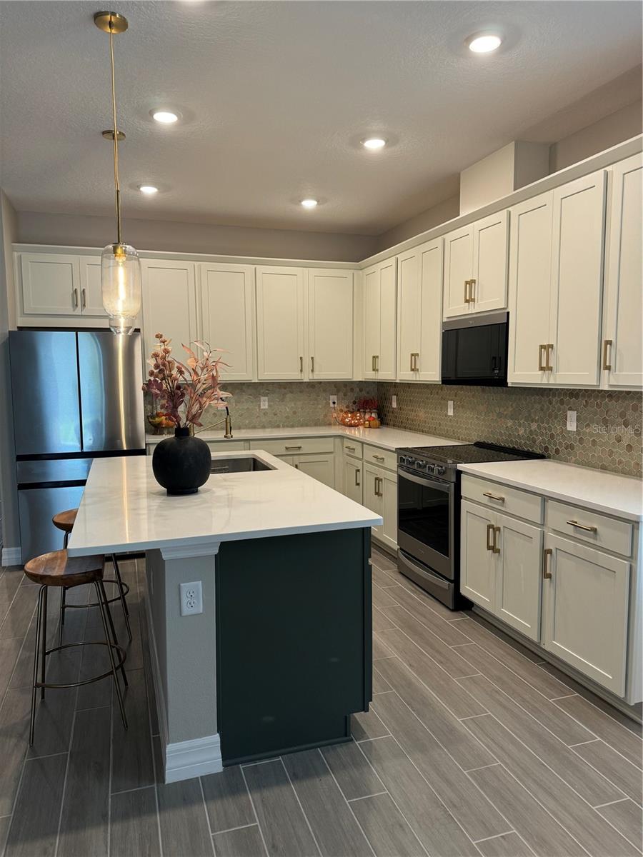 kitchen with white cabinetry, stainless steel appliances, an island with sink, pendant lighting, and wood-type flooring