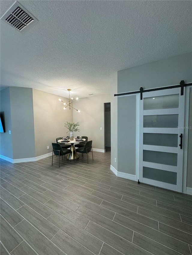 unfurnished dining area featuring a textured ceiling, a barn door, hardwood / wood-style flooring, and a notable chandelier