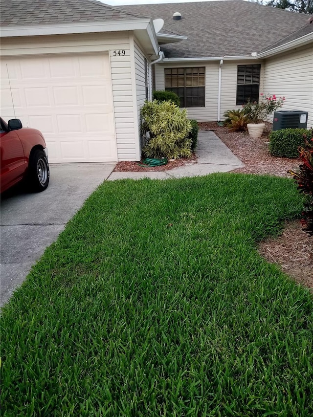 exterior space featuring a garage, a yard, and central AC