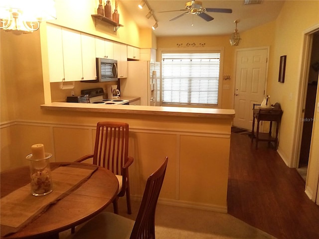 kitchen with kitchen peninsula, track lighting, white appliances, dark wood-type flooring, and white cabinetry