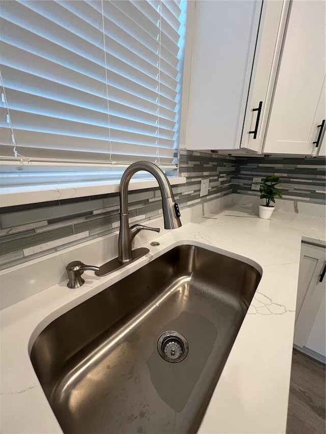 interior details with decorative backsplash, light stone countertops, sink, and white cabinets