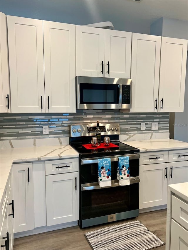 kitchen with white cabinets, light hardwood / wood-style flooring, light stone countertops, appliances with stainless steel finishes, and tasteful backsplash