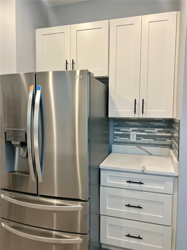 kitchen featuring white cabinets, stainless steel fridge with ice dispenser, decorative backsplash, and light stone countertops