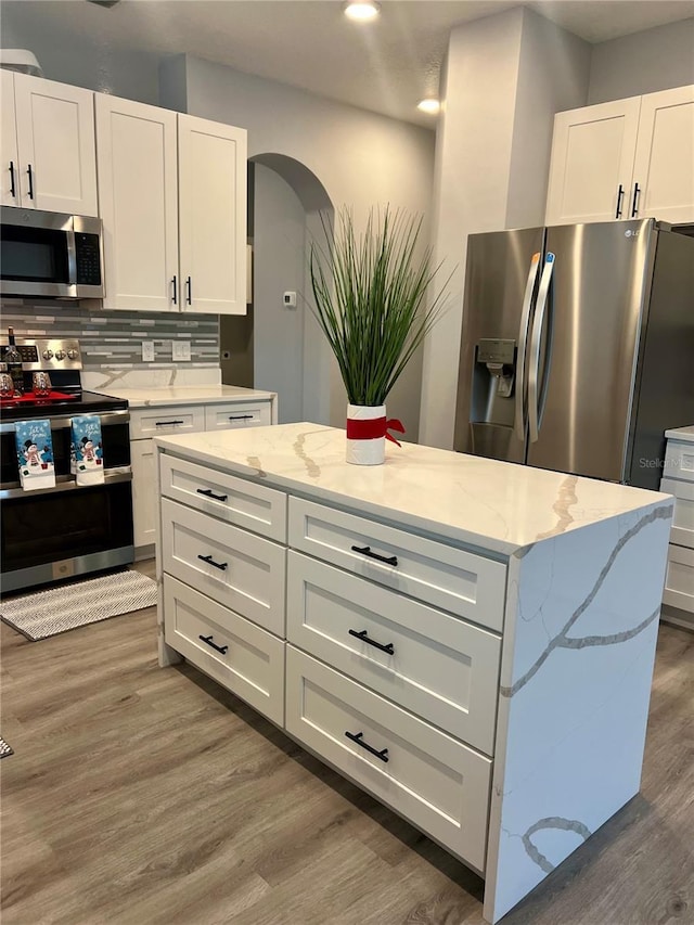 kitchen featuring light stone countertops, dark hardwood / wood-style flooring, tasteful backsplash, stainless steel appliances, and white cabinets