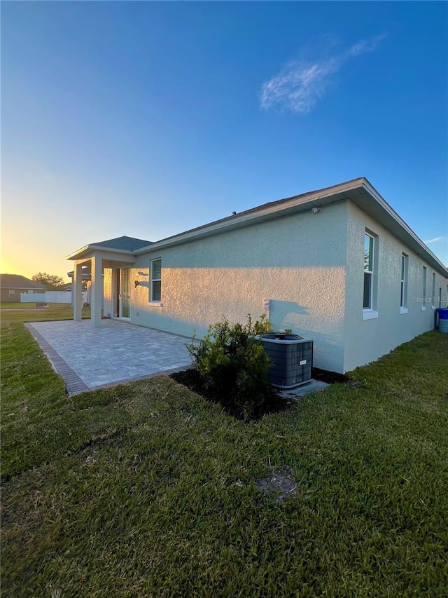 property exterior at dusk with a lawn, a patio area, and central AC