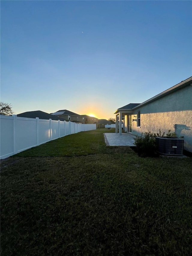 yard at dusk with central AC unit and a patio