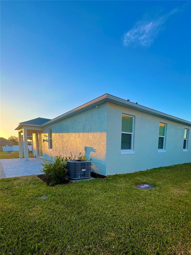 property exterior at dusk featuring a patio area, a yard, and cooling unit