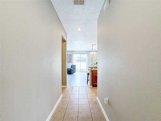 hall with a textured ceiling and light tile patterned floors