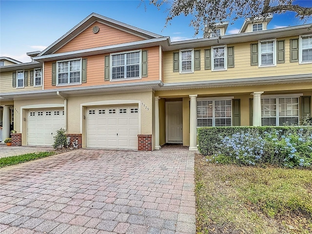 view of property featuring a garage, decorative driveway, brick siding, and stucco siding