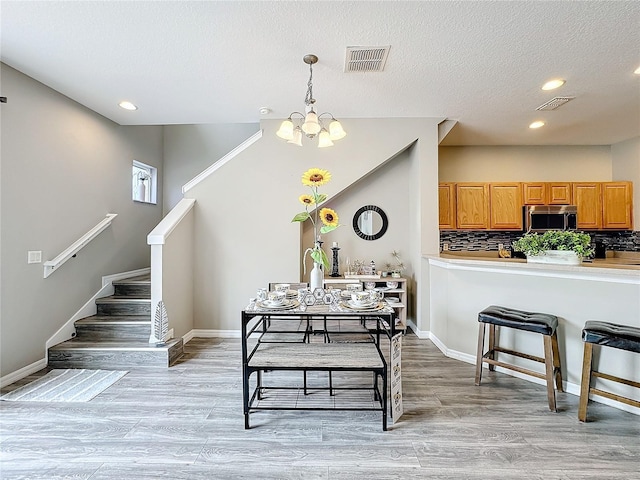 dining area with a textured ceiling, light wood-style flooring, visible vents, baseboards, and stairs