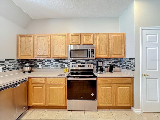 kitchen featuring light tile patterned floors, tasteful backsplash, light countertops, appliances with stainless steel finishes, and light brown cabinets