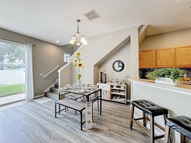 dining space with a chandelier, a textured ceiling, visible vents, light wood-style floors, and stairway