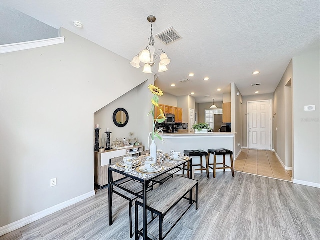 dining room featuring light wood-type flooring, baseboards, visible vents, and a textured ceiling