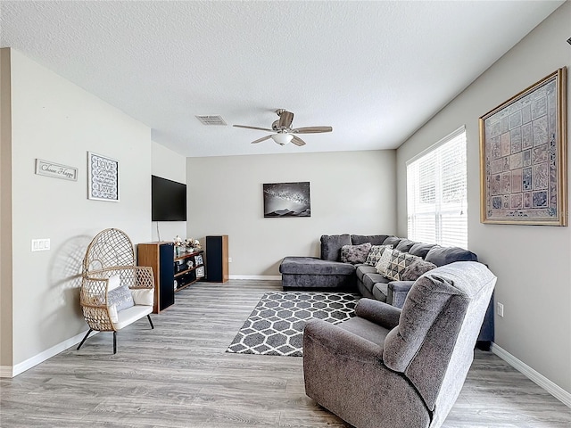 living room featuring visible vents, ceiling fan, a textured ceiling, wood finished floors, and baseboards