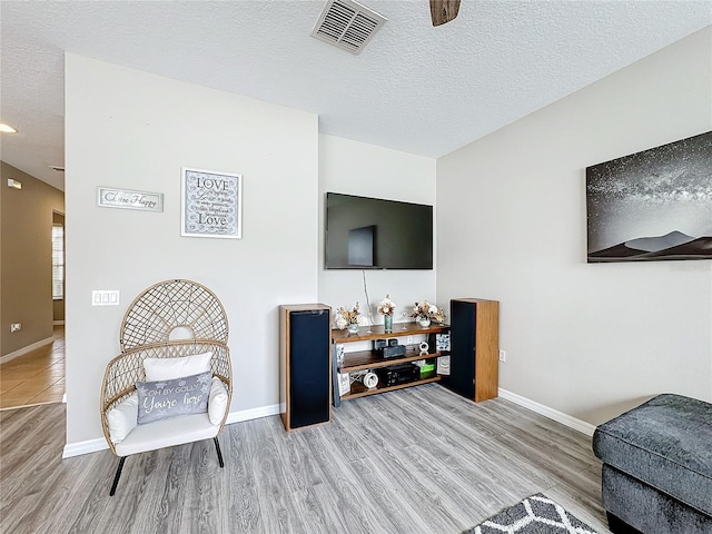 living room with baseboards, a textured ceiling, visible vents, and wood finished floors