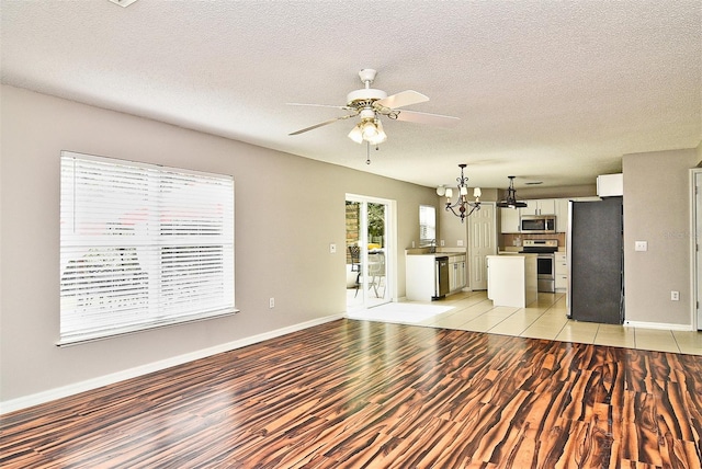 unfurnished living room featuring a textured ceiling, light hardwood / wood-style floors, and ceiling fan with notable chandelier