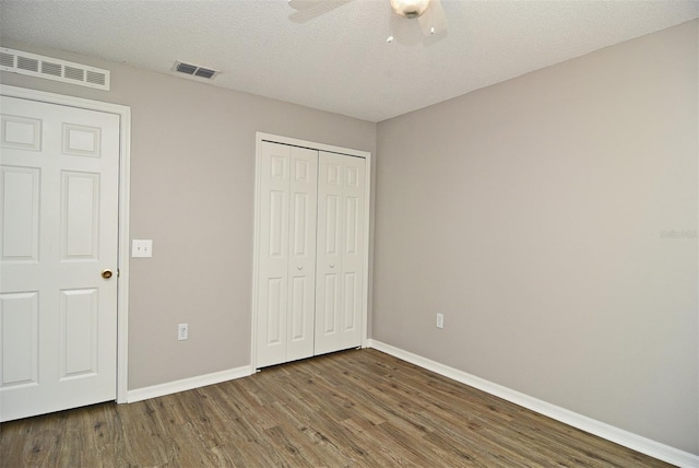 unfurnished bedroom featuring dark wood-type flooring, a closet, a textured ceiling, and ceiling fan