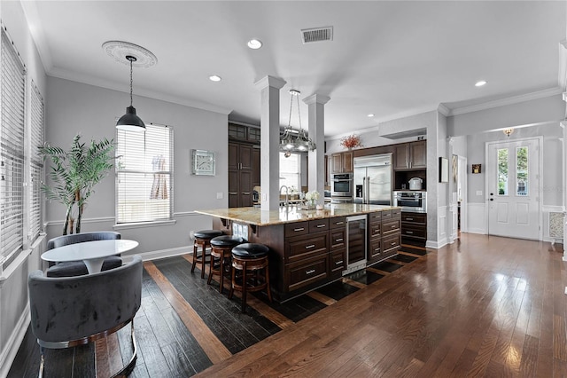 kitchen featuring ornate columns, a kitchen bar, beverage cooler, a kitchen island, and appliances with stainless steel finishes