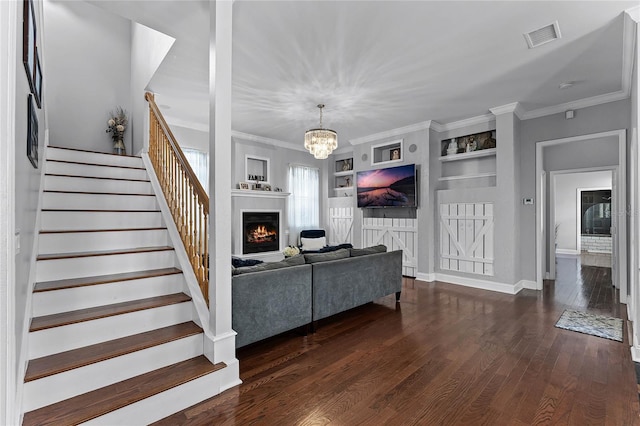 living room featuring dark wood-type flooring, built in features, an inviting chandelier, and crown molding