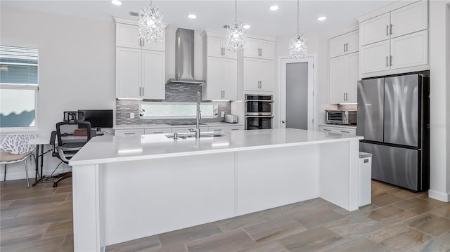 kitchen featuring white cabinetry, wall chimney range hood, decorative light fixtures, and stainless steel appliances