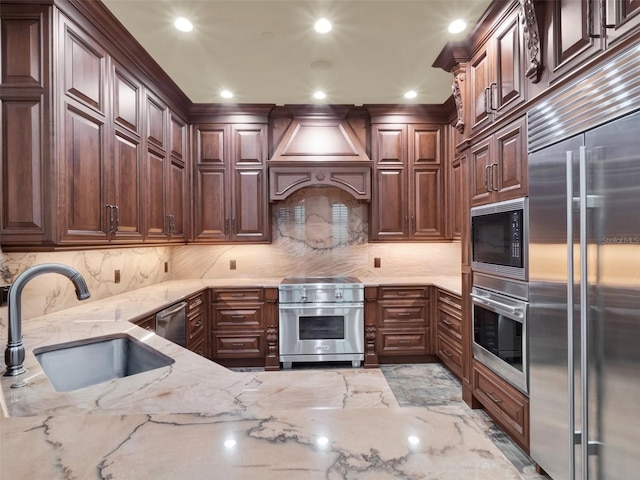 kitchen with a sink, built in appliances, light stone countertops, and custom range hood