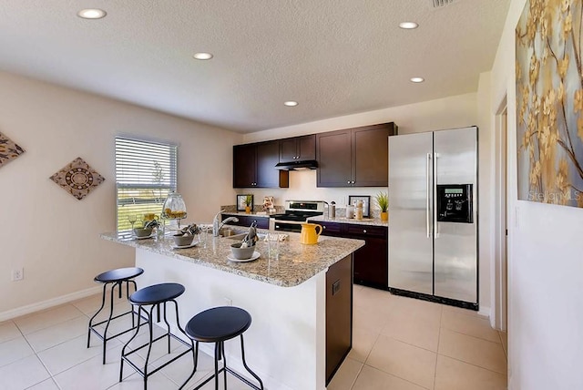 kitchen with dark brown cabinetry, a textured ceiling, a kitchen island with sink, and appliances with stainless steel finishes