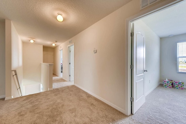 hall with light colored carpet and a textured ceiling