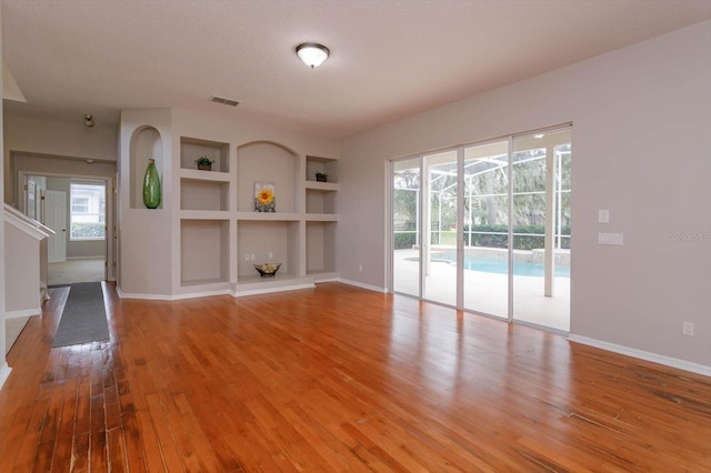 unfurnished living room with built in features, wood-type flooring, and a textured ceiling