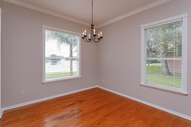 spare room with ornamental molding, wood-type flooring, a notable chandelier, and a healthy amount of sunlight