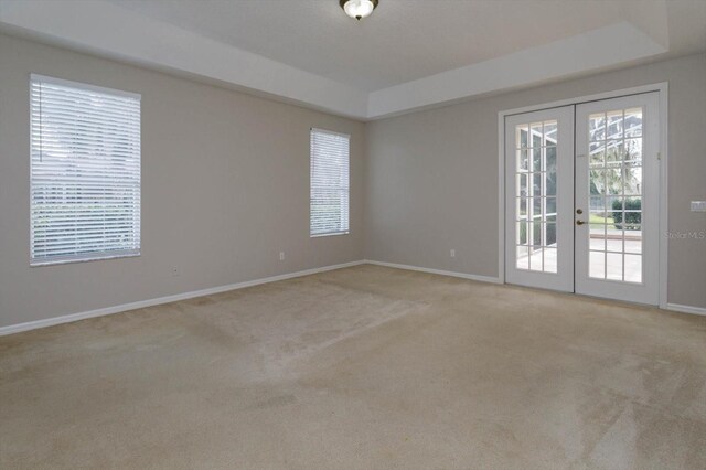 empty room featuring light carpet, french doors, and a tray ceiling