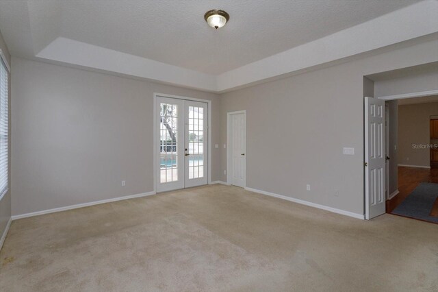 spare room featuring a raised ceiling, light carpet, a textured ceiling, and french doors