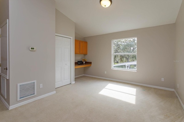 unfurnished living room featuring built in desk, light colored carpet, and vaulted ceiling