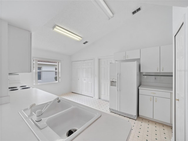 kitchen with vaulted ceiling, white cabinets, a textured ceiling, sink, and white refrigerator with ice dispenser