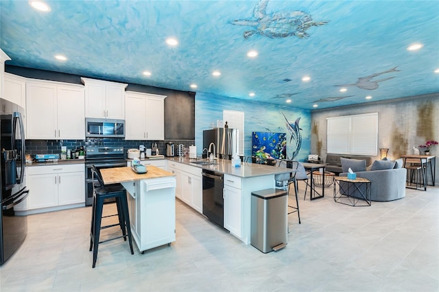 kitchen featuring white cabinets, a breakfast bar, a kitchen island with sink, and appliances with stainless steel finishes