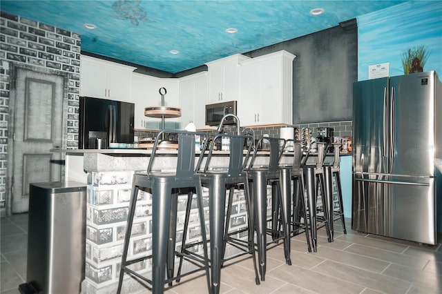 kitchen featuring stainless steel refrigerator, white cabinetry, black fridge, decorative backsplash, and light tile patterned floors