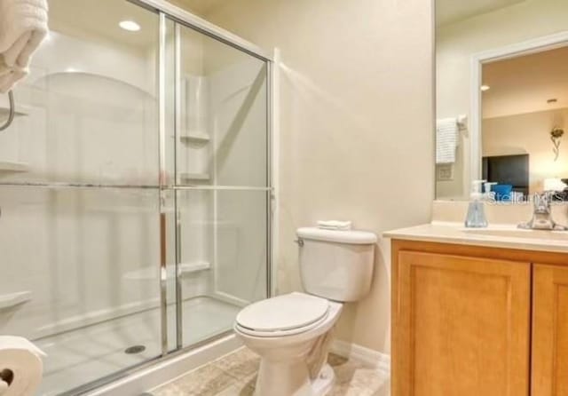 bathroom featuring toilet, vanity, tile patterned flooring, and a shower with door