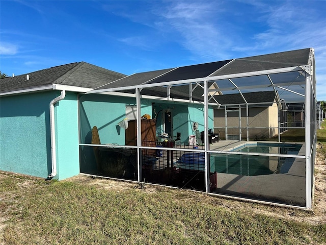 rear view of house featuring a lawn, glass enclosure, and a patio