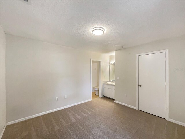 unfurnished bedroom with sink, a textured ceiling, light carpet, and ensuite bathroom