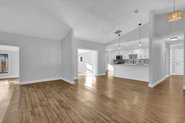 unfurnished living room with wood-type flooring, a textured ceiling, and high vaulted ceiling