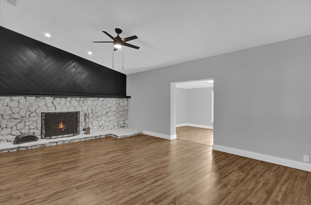 unfurnished living room featuring wood-type flooring, a stone fireplace, and ceiling fan