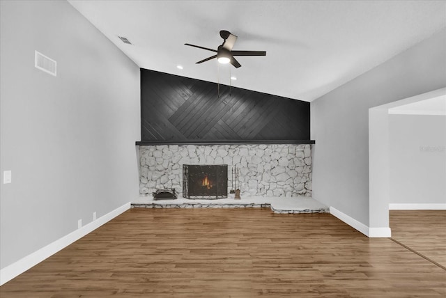 unfurnished living room featuring ceiling fan, a stone fireplace, wood-type flooring, and lofted ceiling