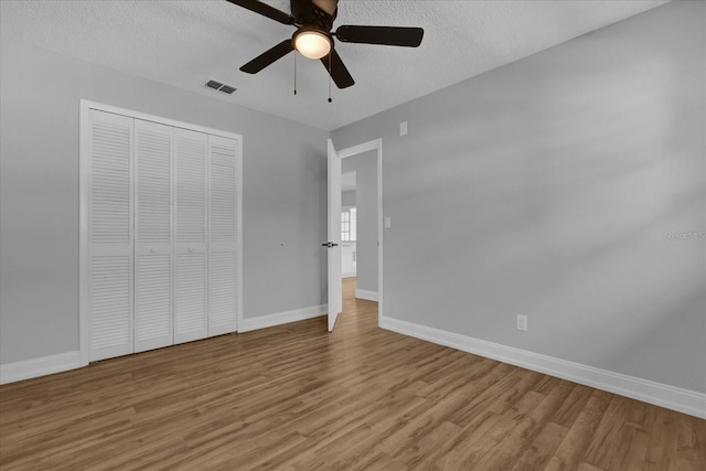 unfurnished bedroom with a textured ceiling, light wood-type flooring, a closet, and ceiling fan