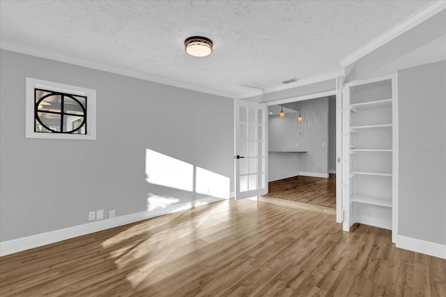 empty room with hardwood / wood-style floors, french doors, crown molding, built in features, and a textured ceiling