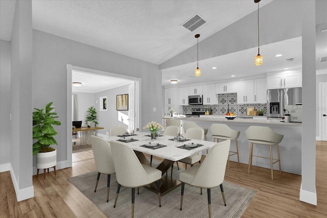 dining room featuring a textured ceiling, light hardwood / wood-style floors, and high vaulted ceiling