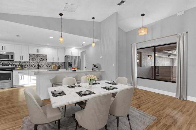 dining space with sink, high vaulted ceiling, and light wood-type flooring