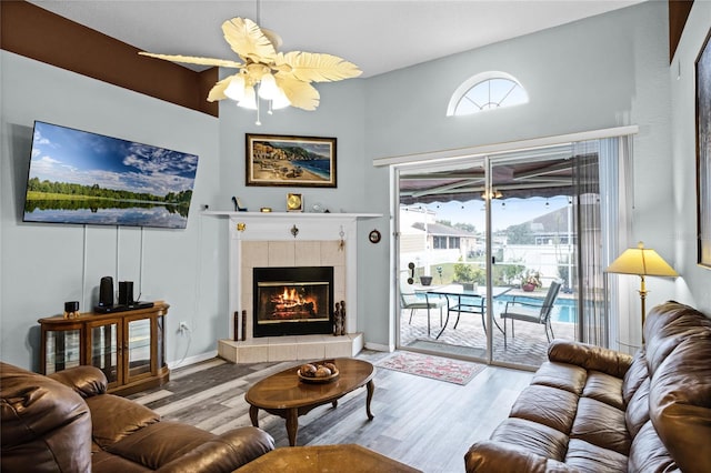 living room with light hardwood / wood-style flooring, ceiling fan, and a tile fireplace