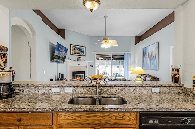 kitchen with sink, light stone counters, ceiling fan, a tile fireplace, and dishwasher