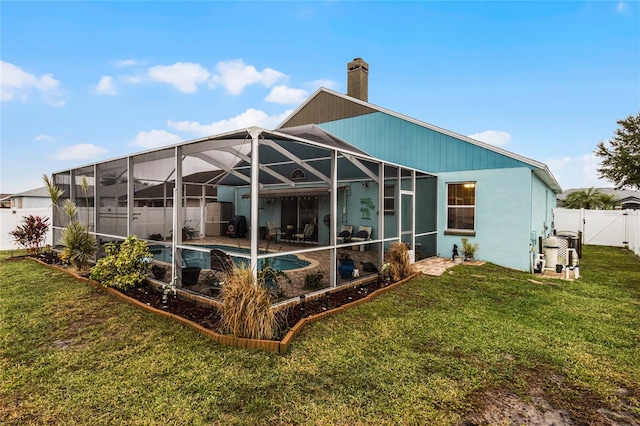 rear view of house featuring glass enclosure, a lawn, and a fenced in pool